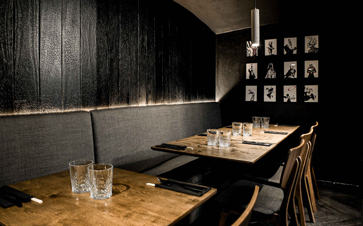 A inimate seating area of tables with benches set against dark textured wood walls