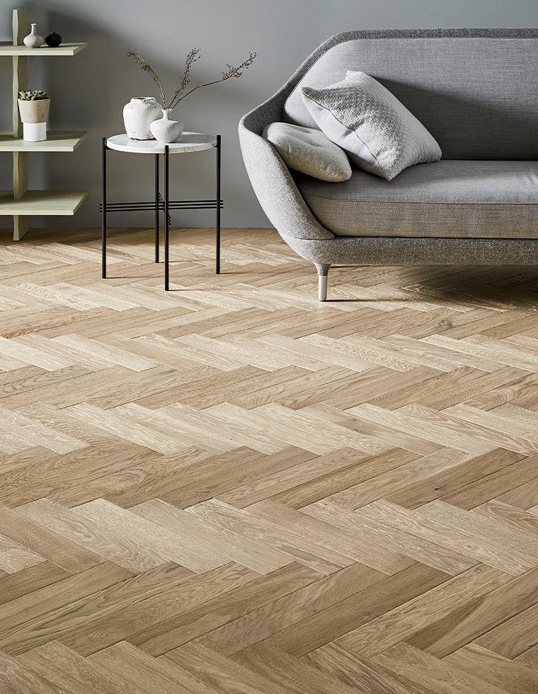 Raw Cotton Herrngbone wood floor showing grey sofa, and white/blck side table