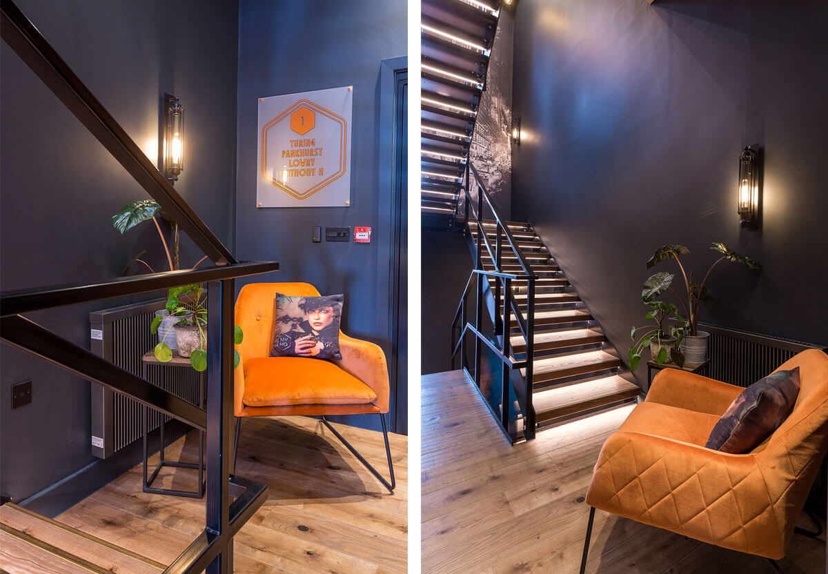 Inside MyHQ. Stariwell, dark blue walls, wall lighting and orange armchair