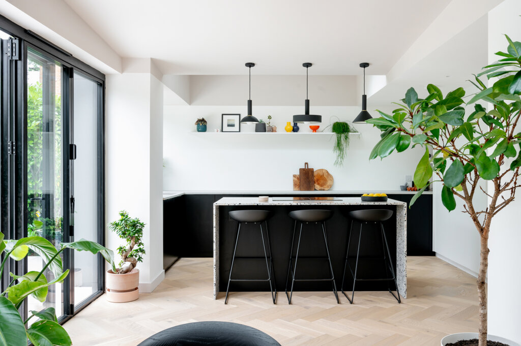 Open plan kitchen renovation with Paperback Herringbone flooring, black kitchen units, terazzo countertops and lots of greenary